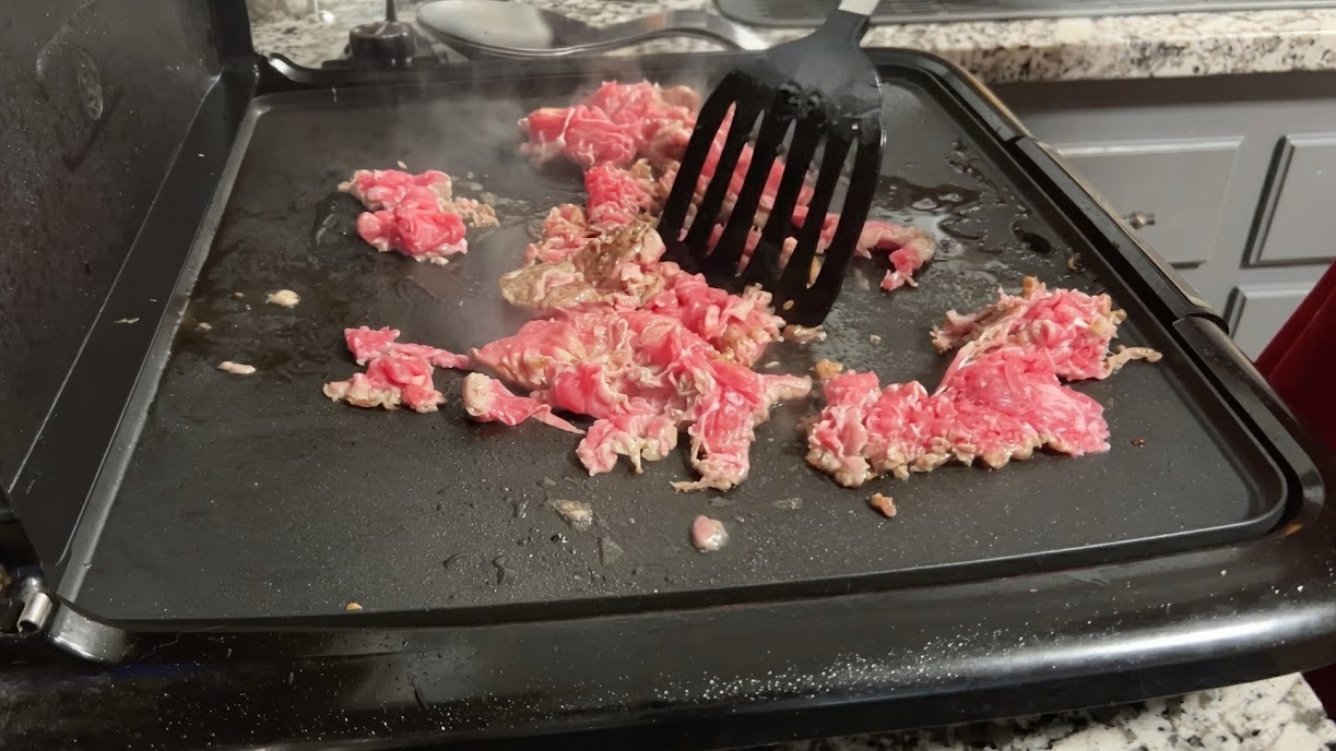 Shaved steak chopped and cooking on the griddle